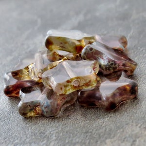 May include: A group of star-shaped glass beads in shades of purple, brown, and gold. The beads are translucent and have a speckled appearance.
