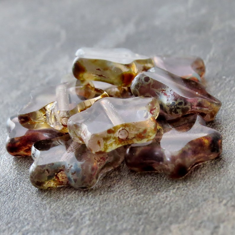 May include: A group of star-shaped glass beads in shades of purple, brown, and gold. The beads are translucent and have a speckled appearance.