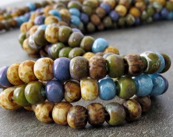 May include: Close-up of a multi-strand necklace made of small, colorful ceramic beads. The beads are in shades of brown, green, blue, and white. The necklace is arranged in a wave-like pattern.