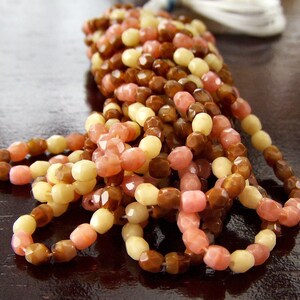 May include: A strand of multi-colored beads in shades of brown, pink, and cream. The beads are faceted and have a slightly irregular shape.