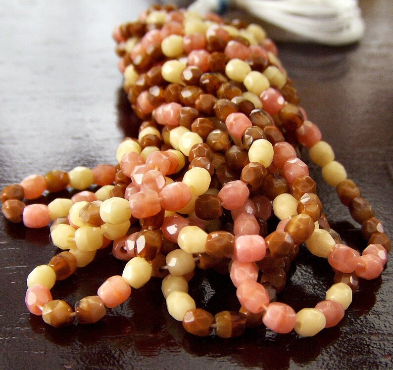 May include: A strand of multi-colored beads in shades of brown, pink, and cream. The beads are faceted and have a slightly irregular shape.