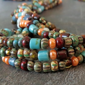 May include: Multi-strand beaded necklace featuring turquoise, brown, orange, and green beads. The necklace is crafted from small, round beads and has a layered, bohemian style.