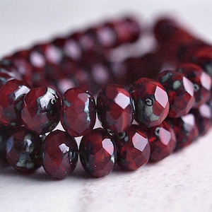 May include: A strand of dark red glass beads with a faceted finish. The beads have a subtle marbled effect with hints of black and white.
