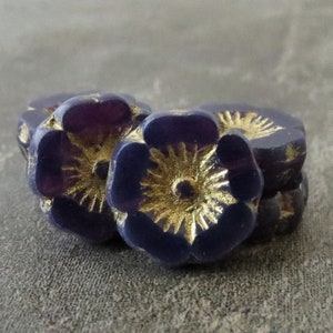 May include: Three purple glass flower beads with gold accents. The beads are stacked on top of each other.