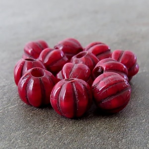 Puede incluir: Un grupo de cuentas redondas de plástico rojo con textura acanalada. Las cuentas tienen un diámetro de aproximadamente 2,5 cm.