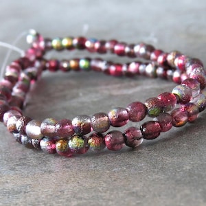 May include: A strand of iridescent pink glass beads with a textured surface. The beads are strung on a clear thread.