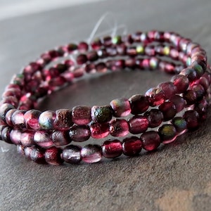 May include: A close-up of a multi-strand bracelet made of small, iridescent, burgundy-colored glass beads.