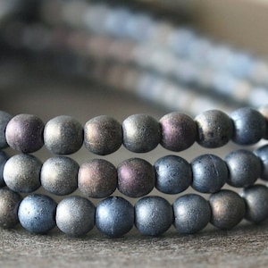 以下が含まれることがあります： 光沢のあるグレーのマットな丸いビーズのストランド。ビーズは円形に配置され、重ねられた効果を生み出しています。