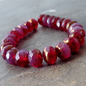 May include: A strand of faceted glass beads in a deep red color with a gold metallic sheen. The beads are strung on a clear thread.
