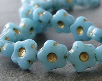 May include: A strand of light blue glass beads in the shape of five-pointed stars with gold flecks. The beads are strung on a clear thread.