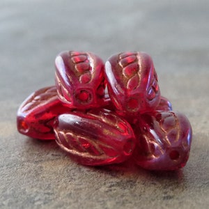 May include: A group of six red glass beads with a gold-colored design. The beads are oval-shaped and have a slightly textured surface.
