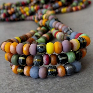May include: A multi-strand necklace made of colourful glass beads. The beads are in various shapes and sizes, including round, oval, and square. The colours of the beads include orange, yellow, green, blue, purple, and brown.