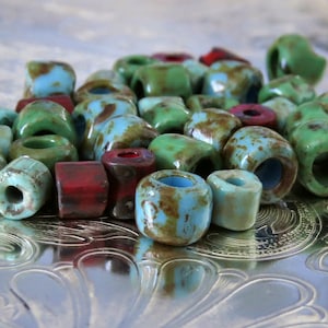May include: A collection of colorful glass beads in shades of blue, green, and red. The beads are round and have a speckled, rustic appearance.