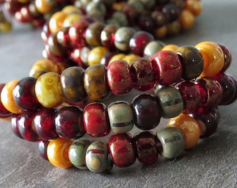 May include: Close-up of several strands of colorful beads. The beads are a mix of red, yellow, brown, and green. The beads are cylindrical and have a slightly textured surface. The beads are strung together to form bracelets or necklaces.