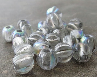 May include: A collection of clear, iridescent glass beads. Each bead is round with a grooved design and a hole for stringing. The beads have a subtle rainbow sheen, reflecting light.