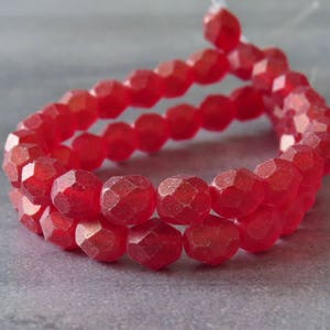 May include: A strand of red faceted glass beads. The beads are round and have a matte finish.