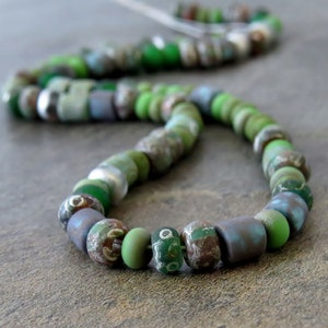 May include: A green, blue, and brown glass bead necklace. The beads are various shapes and sizes, and some have a mottled or textured surface.