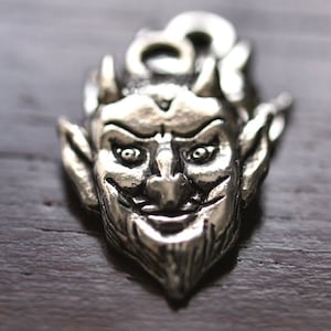 Puede incluir: Encanto de colgante de plata con una representación detallada de la cara de un diablo con cuernos, una nariz puntiaguda y una sonrisa traviesa.