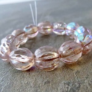 以下が含まれることがあります： ファセット加工が施され、リブ模様が施された虹色のピンク色のガラスビーズのストランド。ビーズは白い糸に通されています。