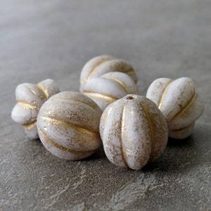 Peut inclure: Six perles en céramique blanche avec des accents dorés. Les perles sont de forme ovale et ont une surface texturée.