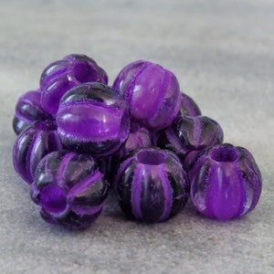 May include: A group of purple and black striped beads. The beads are round and have a textured surface.