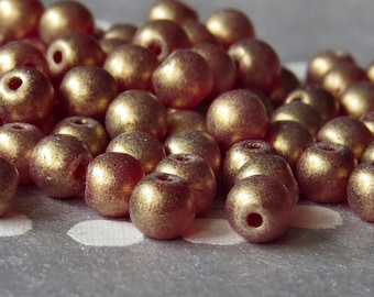 May include: A pile of small, round, metallic beads in a deep red color with a gold sheen.