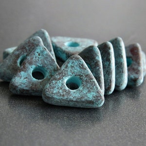 May include: A group of teal and brown triangular ceramic beads with a hole in the center. The beads have a rustic, distressed look.