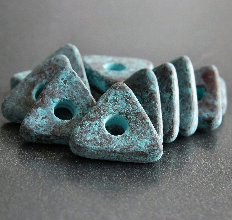 May include: A group of teal and brown triangular ceramic beads with a hole in the center. The beads have a rustic, distressed look.