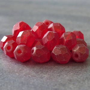 May include: A pile of red faceted glass beads. The beads are translucent and have a slightly frosted finish.