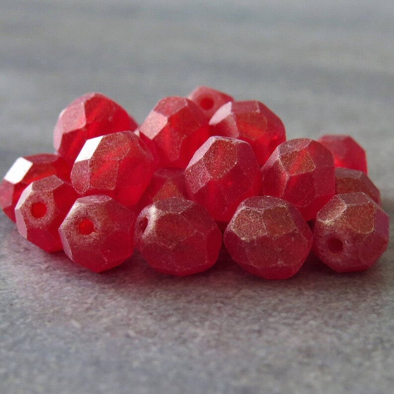 May include: A pile of red faceted glass beads. The beads are translucent and have a slightly frosted finish.