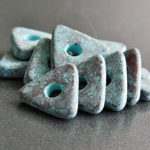 May include: A group of teal blue triangle-shaped ceramic beads with a hole in the center of each bead. The beads have a rustic, distressed look.