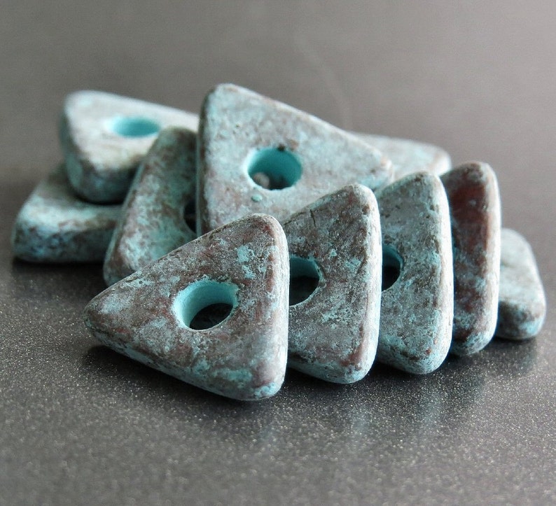 May include: A group of teal blue triangle-shaped ceramic beads with a hole in the center of each bead. The beads have a rustic, distressed look.