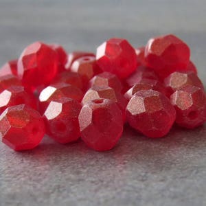 May include: A close-up of a pile of red faceted glass beads. The beads are shiny and have a slightly iridescent finish.