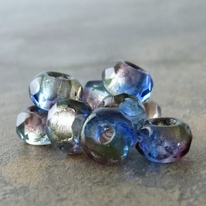 May include: A group of iridescent glass beads in shades of blue, green, and purple. The beads have a faceted, geometric shape and a metallic sheen.