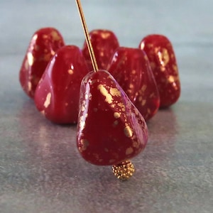 Peut inclure: Six perles de verre rouges avec des paillettes dorées. Les perles sont en forme de poire et ont une finition brillante.