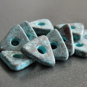May include: A group of teal blue triangle-shaped beads with a hole in the center. The beads have a distressed, aged look with a brown patina.