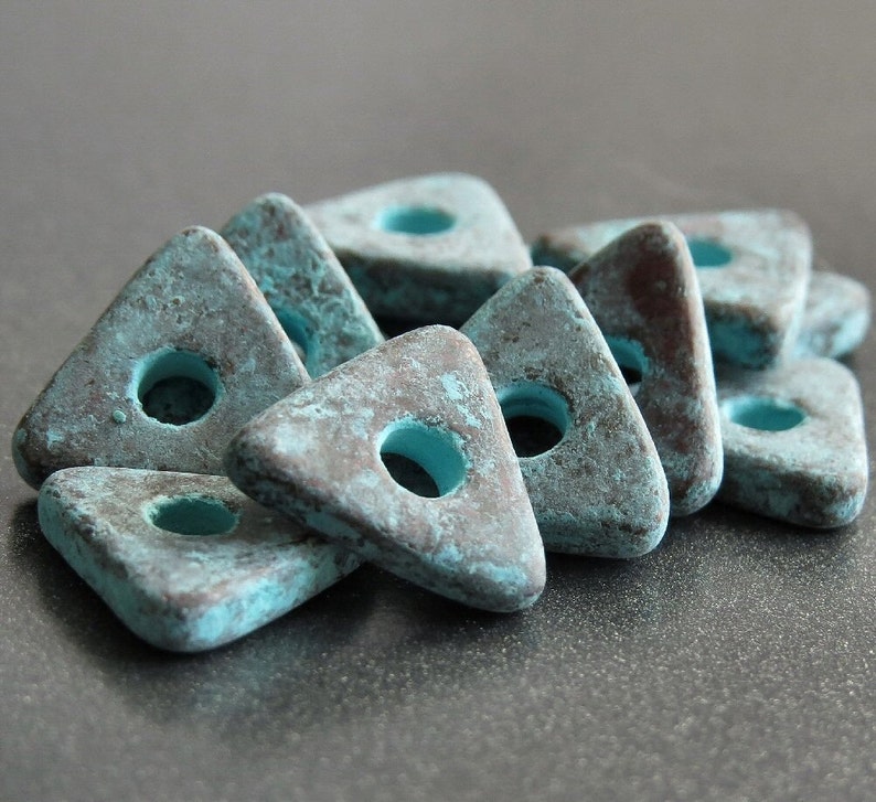 May include: A group of teal blue triangle-shaped beads with a hole in the center. The beads have a distressed, aged look with a brown patina.