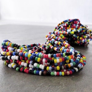 以下が含まれることがあります： カラフルなビーズネックレスのコレクション。ビーズは小さくて丸く、赤、黄、青、緑、白など様々な色があります。ネックレスは絡み合った山に配置され、いくつかのストランドが広がっています。