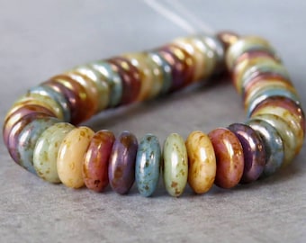 May include: Strand of colorful, iridescent glass beads in a variety of colors including yellow, orange, blue, and purple. The beads are oval-shaped and strung together, creating a circular or curved shape. The beads are on a gray surface.