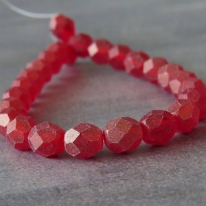 Puede incluir: Una hebra de cuentas de vidrio facetadas rojas. Las cuentas son de color rojo intenso y tienen un acabado ligeramente iridiscente.