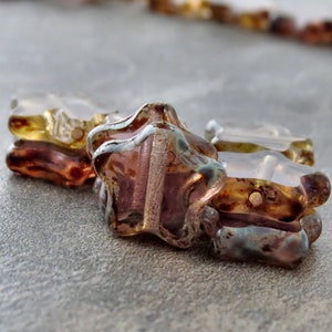 May include: Close-up of iridescent glass star-shaped beads with a brown and purple colour scheme. The beads have a textured surface and are strung together.
