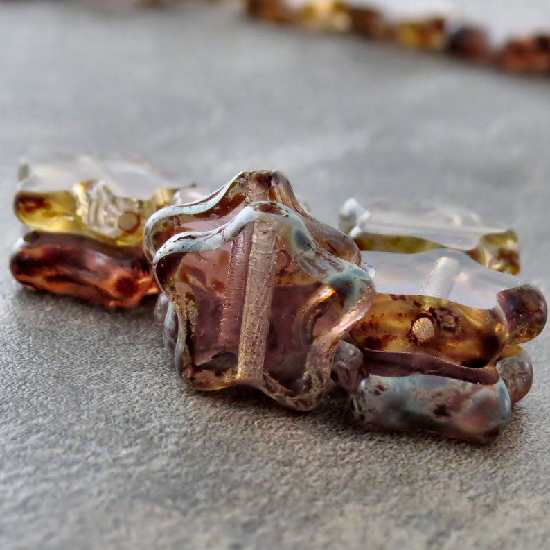 May include: Close-up of iridescent glass star-shaped beads with a brown and purple colour scheme. The beads have a textured surface and are strung together.