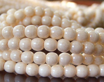 May include: Close-up of strands of cream-coloured, round beads. The beads are smooth and evenly sized, reflecting light. The background is blurred, suggesting a focus on the jewellery.