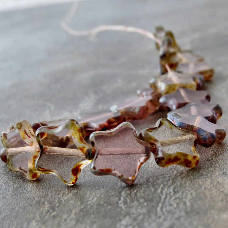 May include: A strand of star-shaped glass beads in shades of brown, pink, and clear. The beads have a mottled, textured surface.