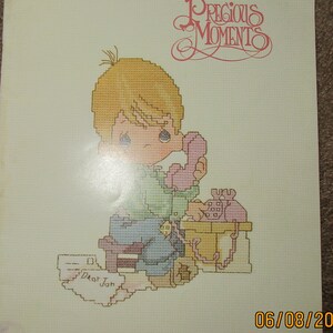 May include: A cross-stitch pattern book titled "Precious Moments" featuring a child on the phone. The cover includes the text "Dear Jon" and the date 06/08/20. The design is by Gloria & Pat.