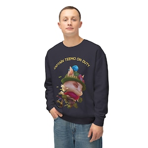 May include: Navy blue sweatshirt featuring a cartoon character wearing a green hat and a red scarf. The text "CAPTAIN TEEMO ON DUTY" is printed above the character. The sweatshirt is made of a soft material.
