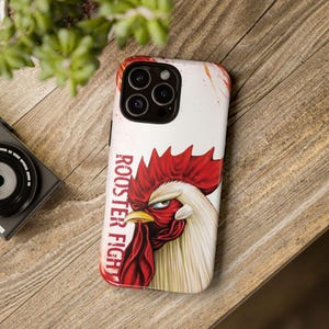 May include: A white phone case featuring a detailed illustration of a rooster's head with red comb and wattle, and a yellow beak. The text "ROOSTER FIGHT" is printed vertically in red. The case has a glossy finish.