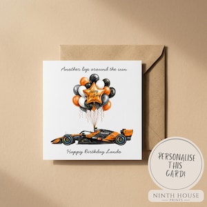 May include: A square greeting card featuring a black and orange Formula 1 race car lifting a cluster of black, white, and orange balloons. The text reads Another lap around the sun and Happy Birthday Lando. A brown envelope is positioned behind the card.
