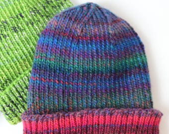 May include: Two knitted beanies. One is a vibrant green with flecks of darker green. The other beanie is a mix of colors, including blue, purple, green, and red. The brim of the second beanie is a deep pink color.