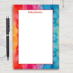 May include: A blank notepad with a watercolor border in shades of orange, pink, purple, and blue. The notepad has a red border and the name "Emily Johnson" printed in red at the top.